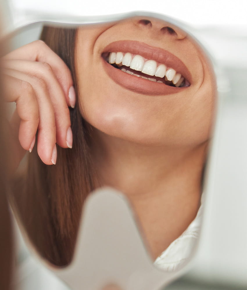 Close-up of a woman's smiling mouth reflected in a hand mirror showing her white teeth