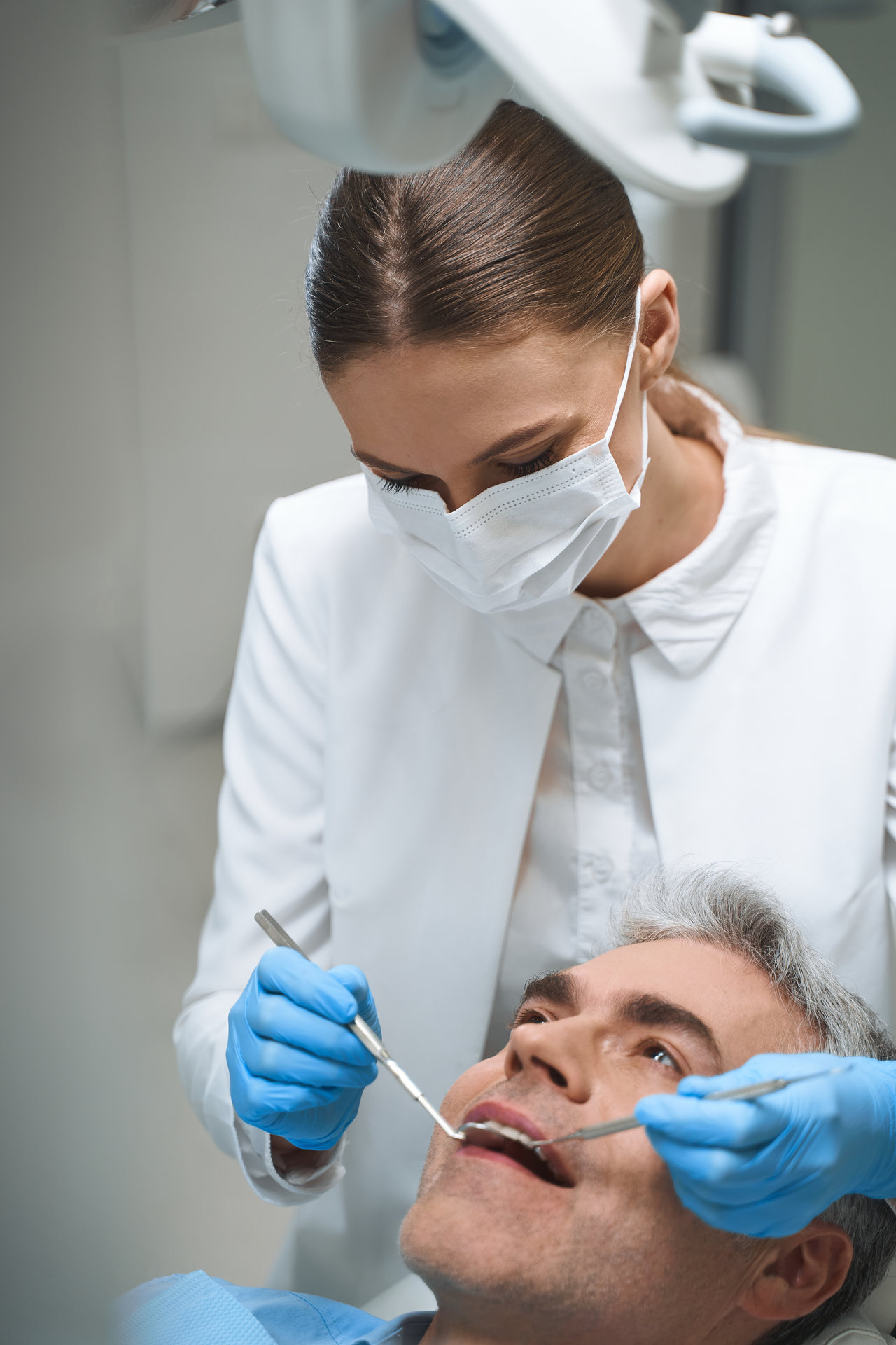 Male is lying in dental chair while woman in sterile mask is helping him solve problems with teeth