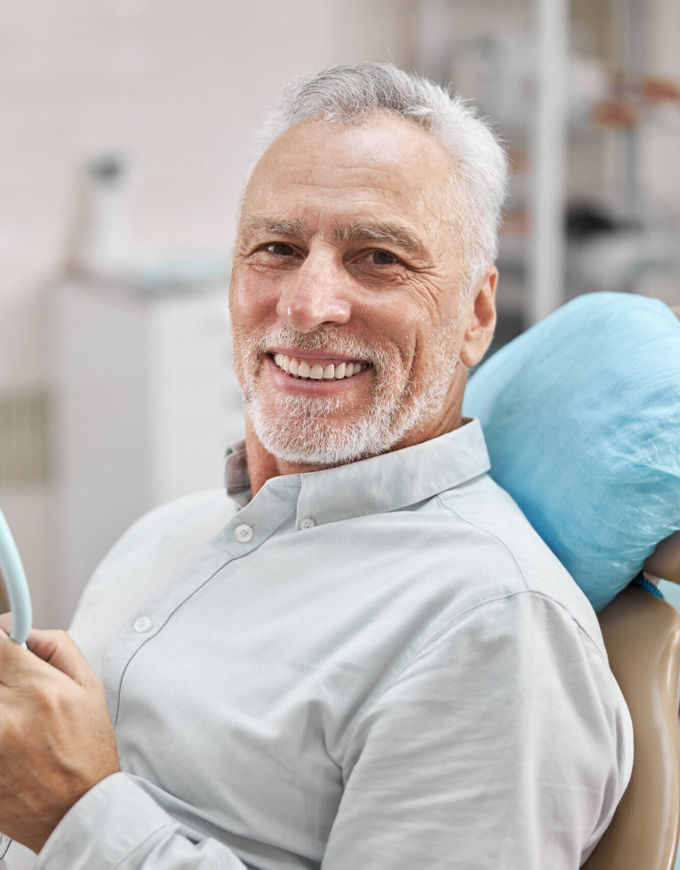 Cheerful patient sitting in a dental chair and holding a mirror while smiling at the camera