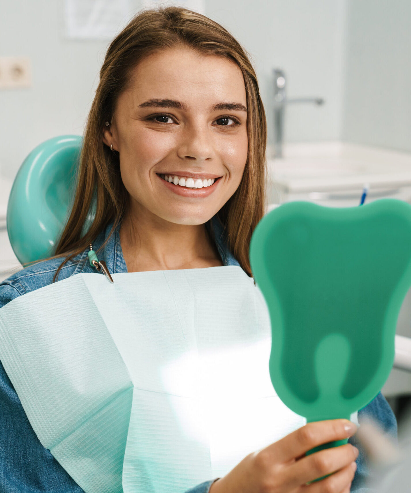 European young woman smiling while looking at mirror in dental clinic