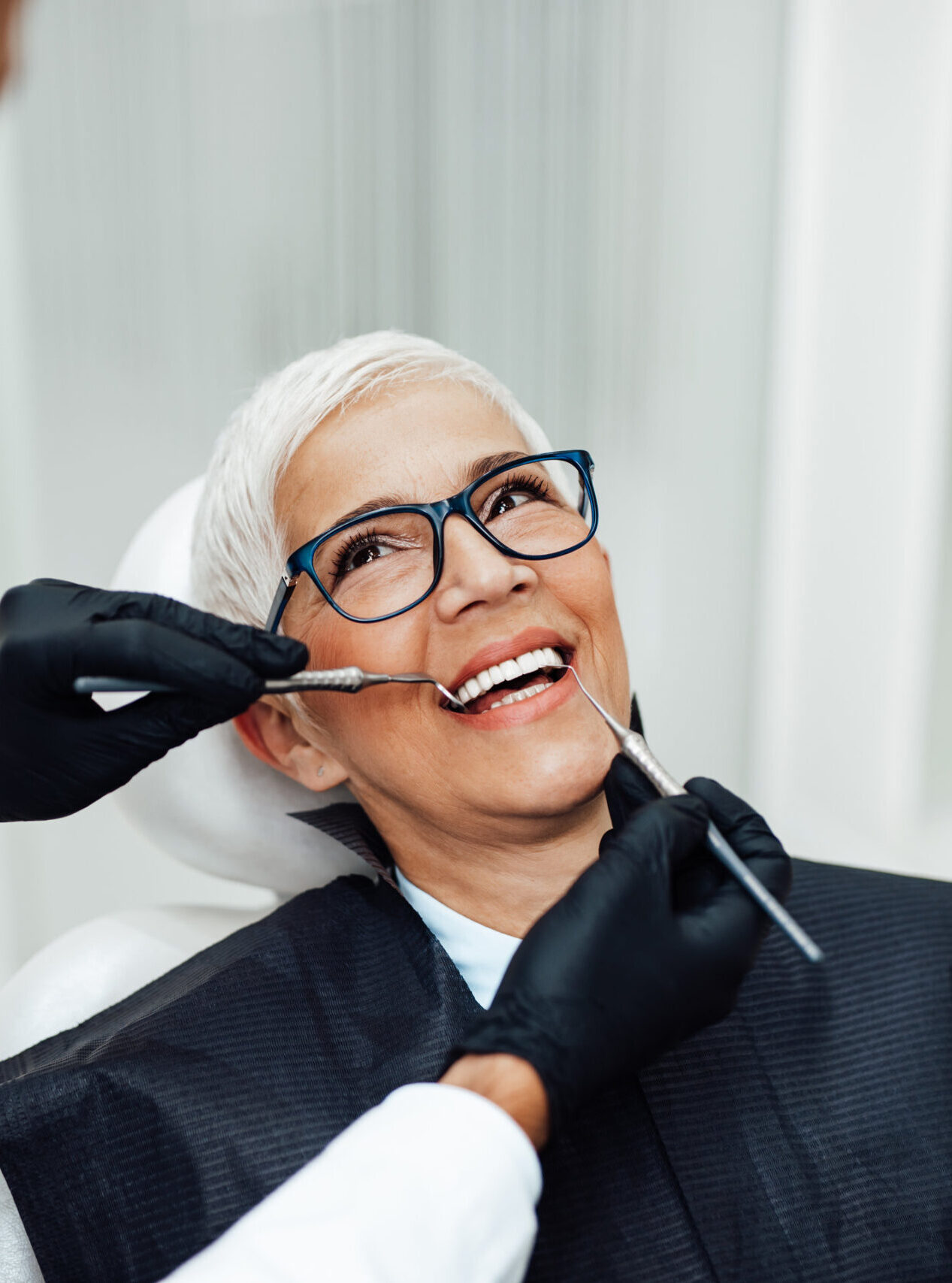 Beautiful senior woman having dental treatment at dentist's office. Dentist is wearing protective face mask due to coronavirus pandemic.