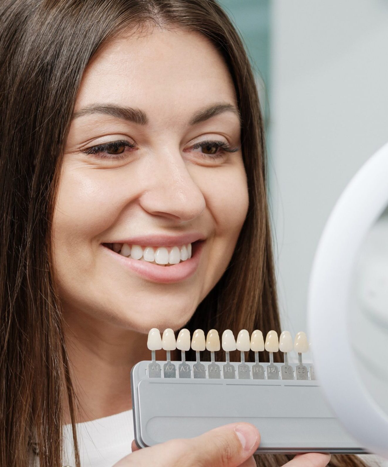 Young man dentist in white coat show veneers enamel color palette for beautiful patient woman