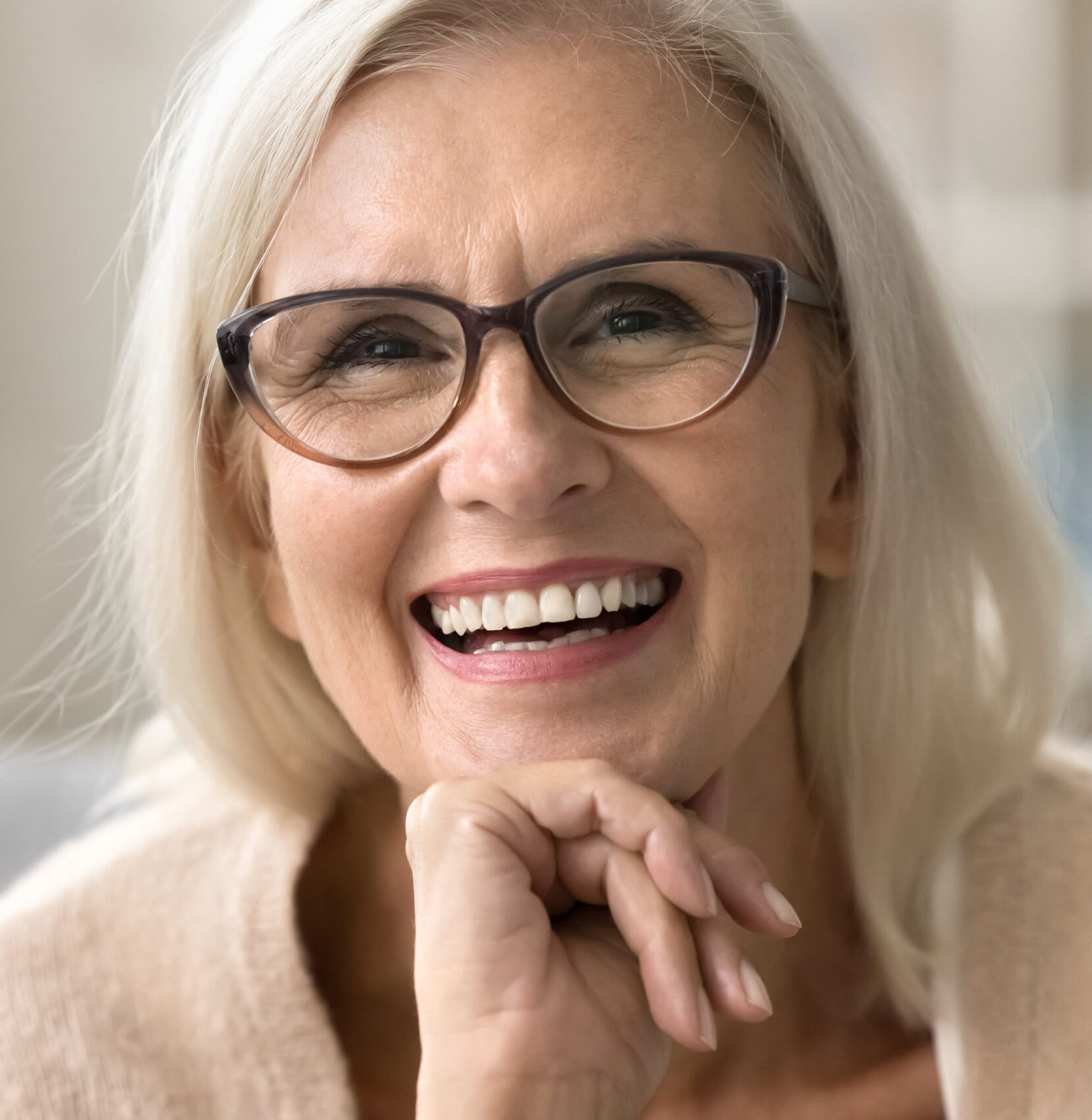 Face of happy senior female model with stylish elegant glasses, toothy smile, fair hair. Cheerful old woman looking at camera for close up portrait, laughing, showing healthy white teeth