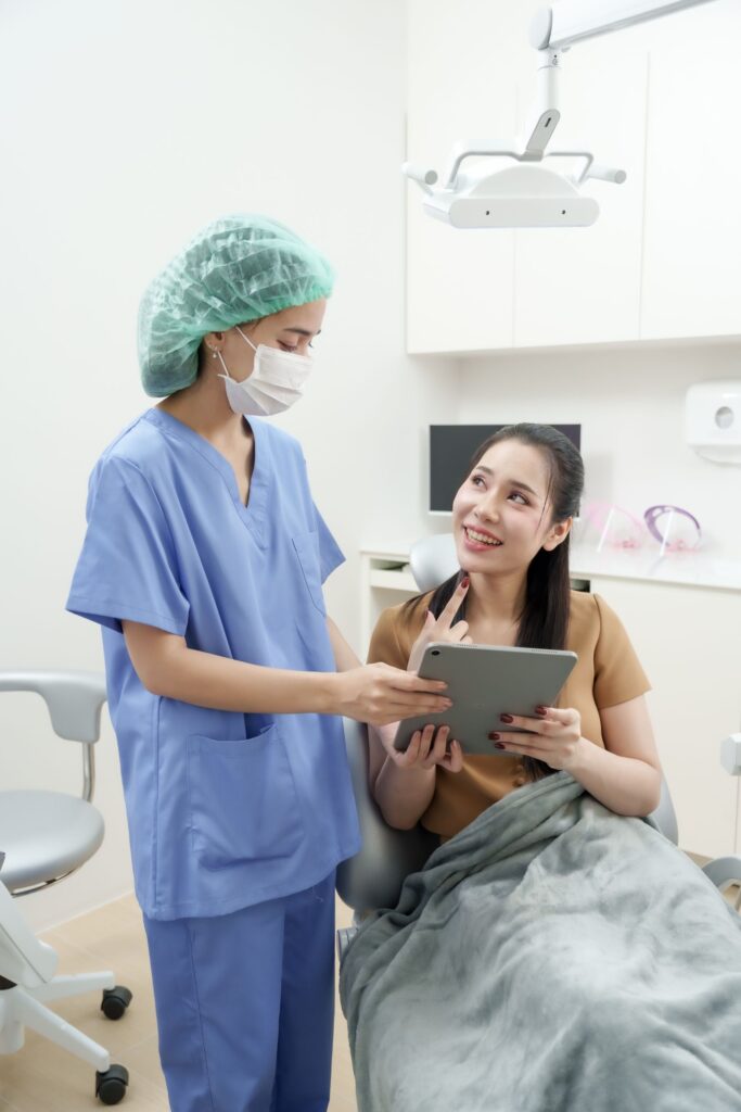 Dental staff member in scrubs and a mask showing a tablet to a smiling patient wrapped in a blanket