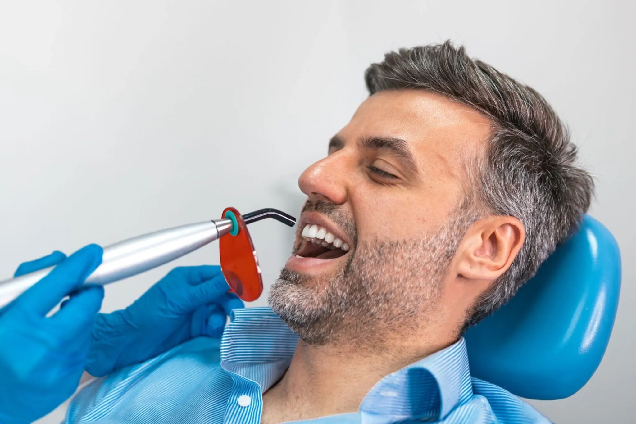 Dentist using a curing light on a smiling male patient's teeth