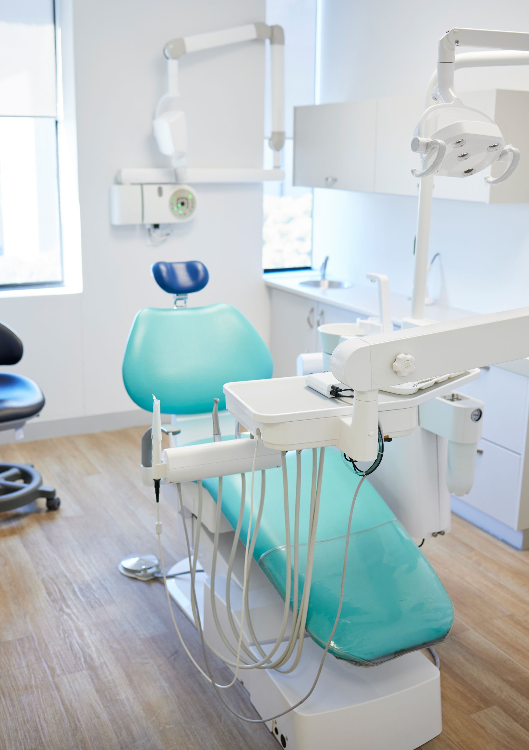 Empty dental treatment room with a teal exam chair and overhead light