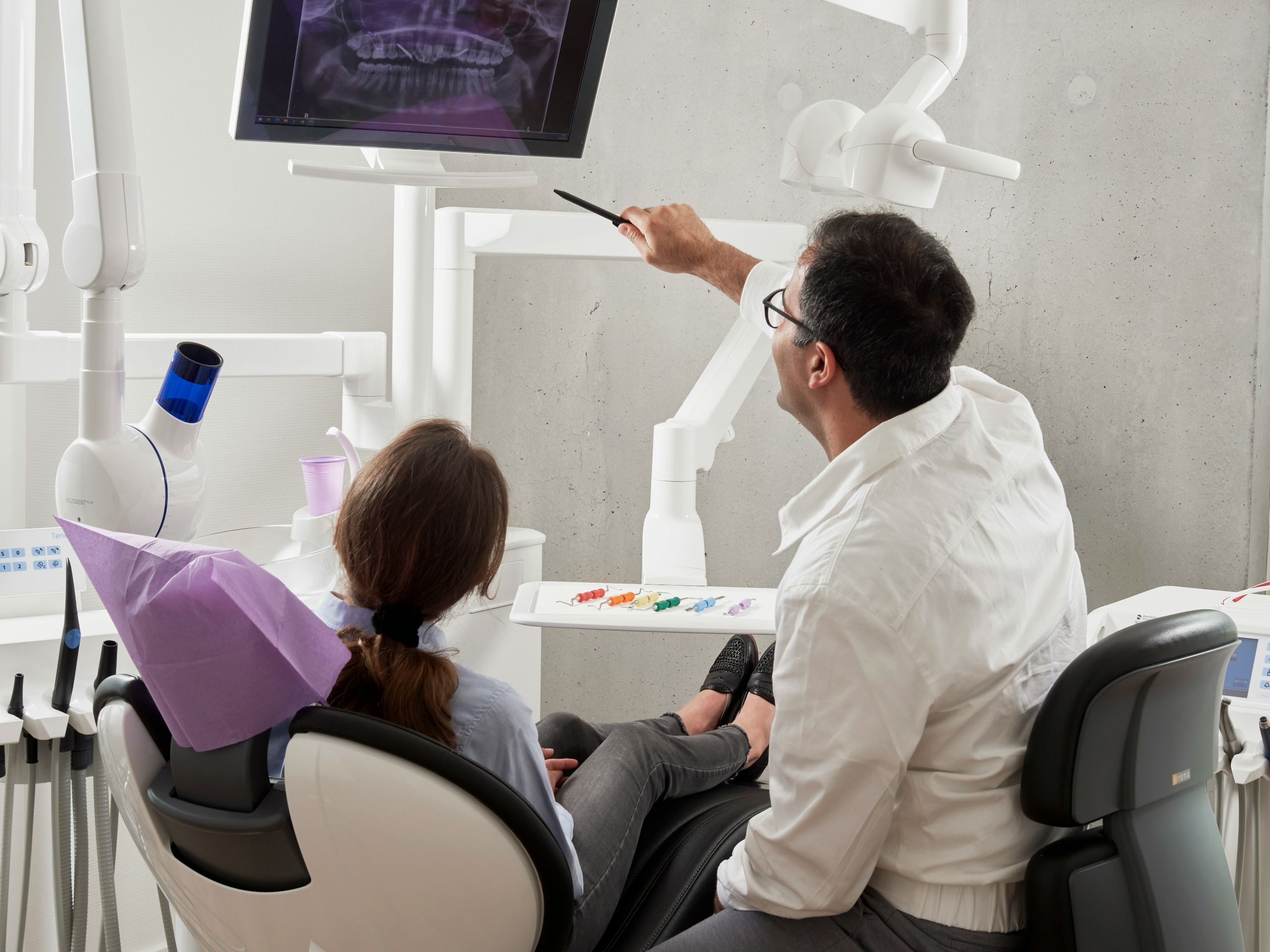 Dentist pointing to a dental X-ray on a monitor while consulting with a seated patient