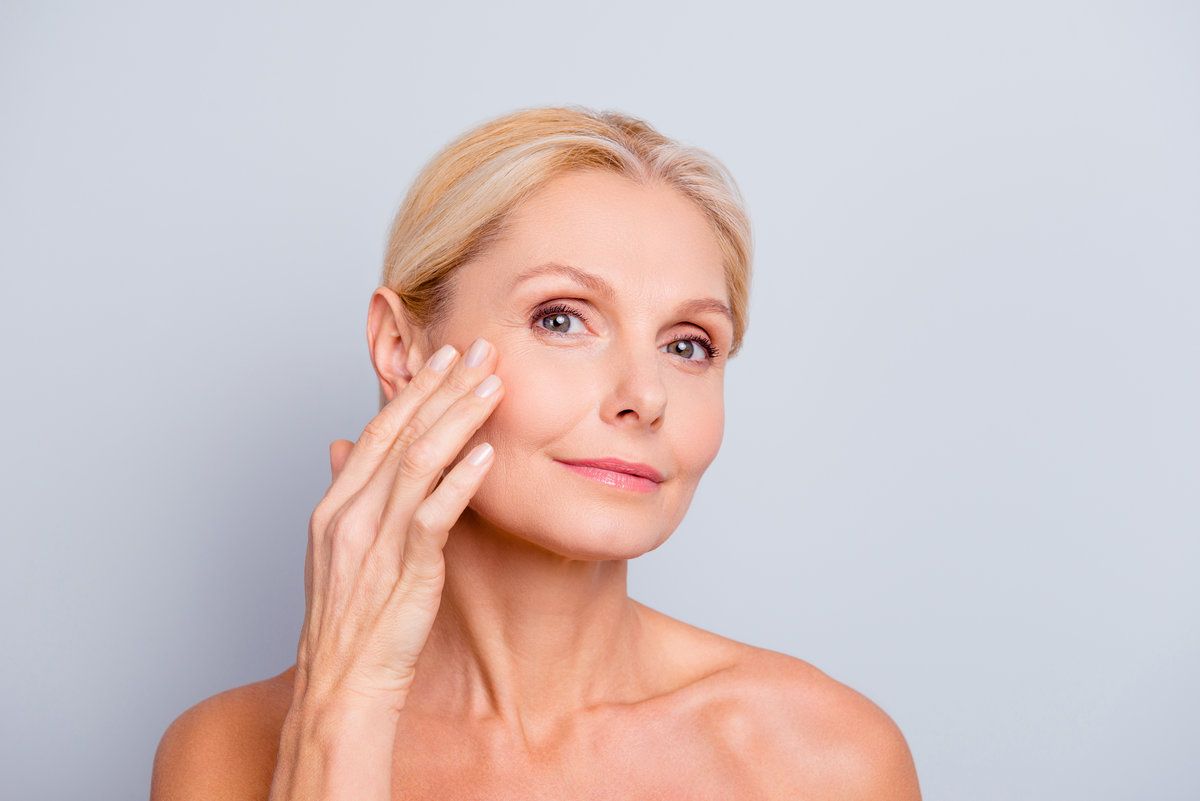 Pretty, charming, attractive woman touching, enjoying her perfect face skin, holding fingers on cheek, pimple, whelk, pustule, dry, oiled, problem skin concept, isolated on grey background