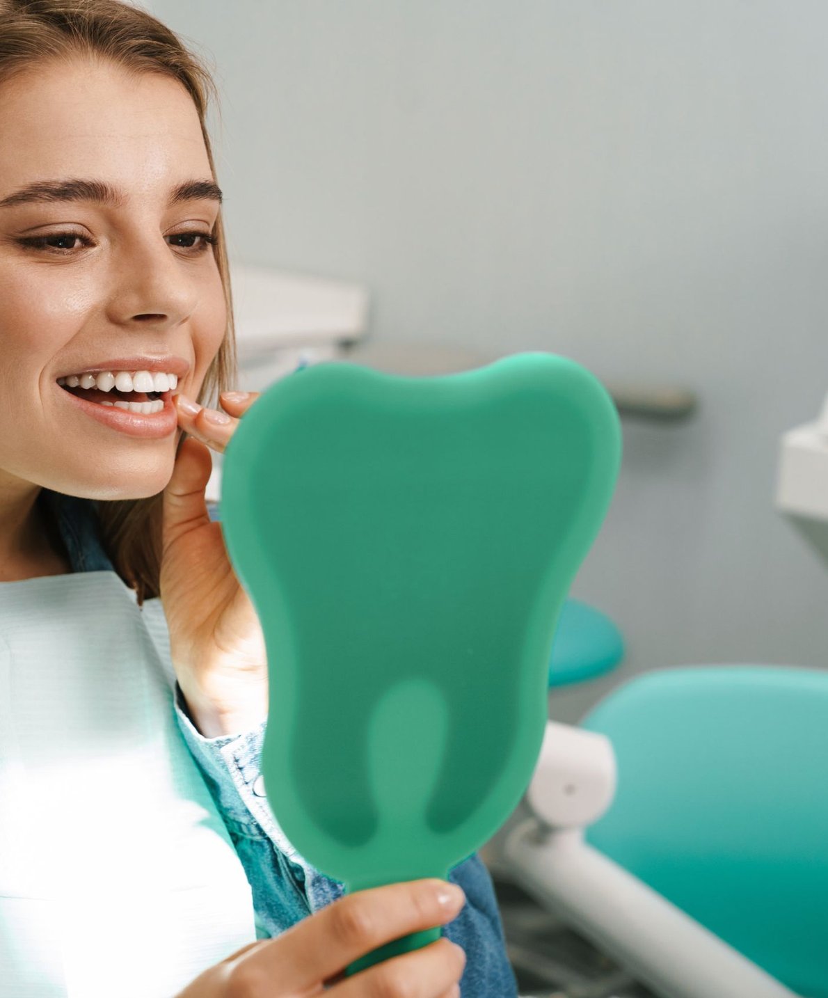 Woman smiling in a dental chair holding a tooth model