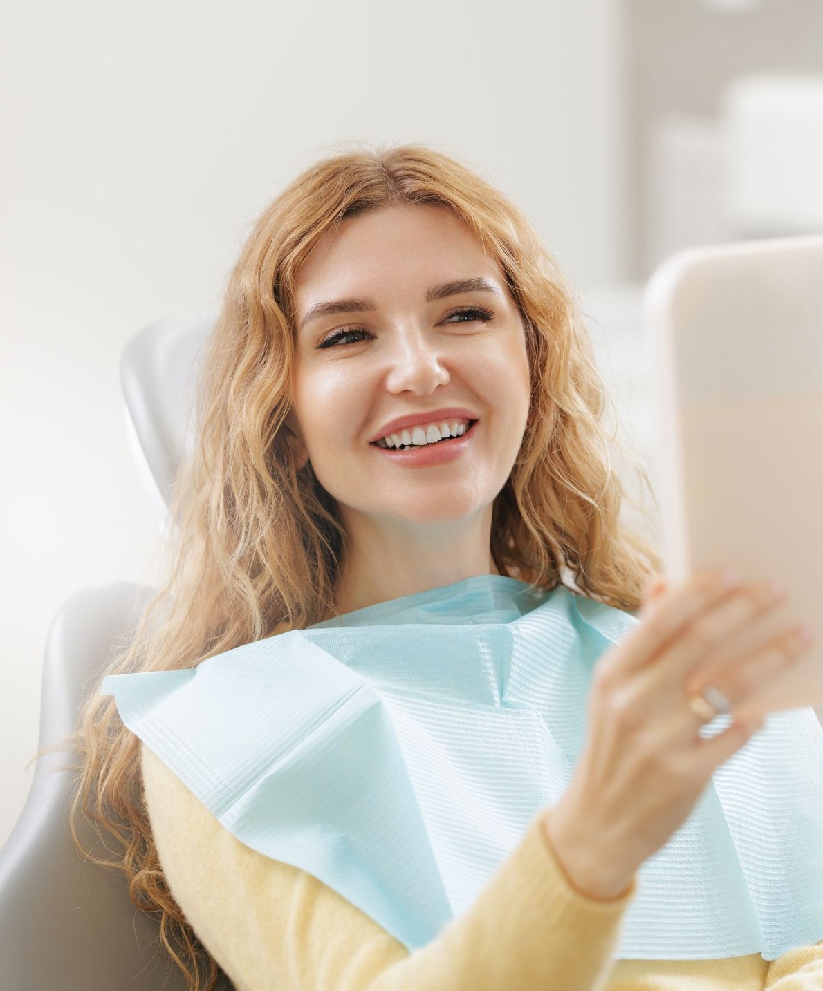 Woman in a dental chair holding a mirror while considering veneers