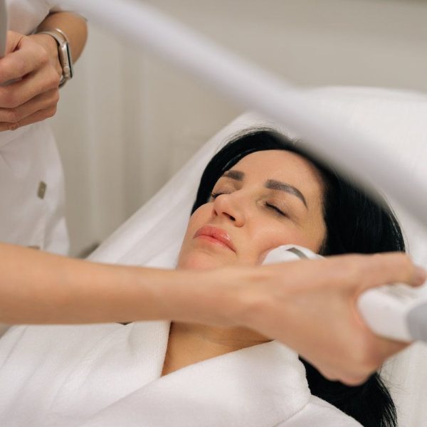 Close-up of relaxed woman with closed eyes receiving microneedle radiofrequency face lifting procedure from dermatologist for skin tightening and rejuvenation in professional aesthetic
